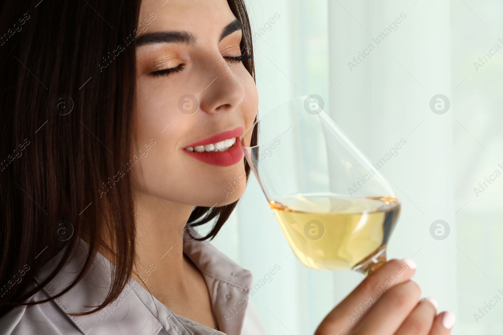 Photo of Beautiful young woman with glass of luxury white wine indoors, closeup. Space copy text