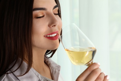 Photo of Beautiful young woman with glass of luxury white wine indoors, closeup. Space copy text