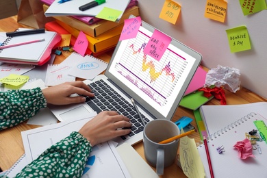 Woman using laptop at messy table, closeup. Concept of being overwhelmed by work