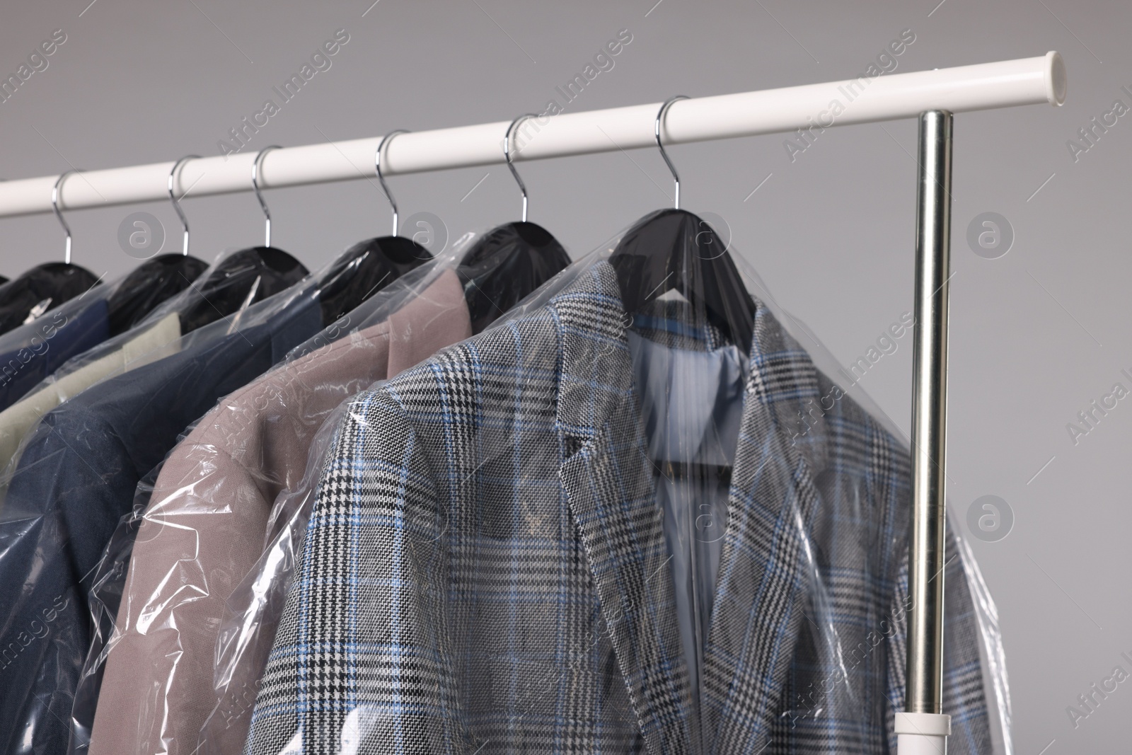 Photo of Dry-cleaning service. Many different clothes in plastic bags hanging on rack against grey background