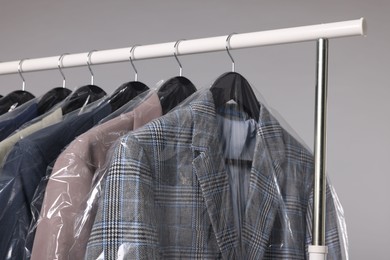 Photo of Dry-cleaning service. Many different clothes in plastic bags hanging on rack against grey background