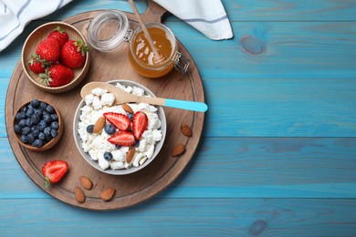 Photo of Bowl of fresh cottage cheese, berries with almond and ingredients on light blue wooden table, flat lay. Space for text