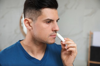 Photo of Man applying hygienic lip balm in bathroom