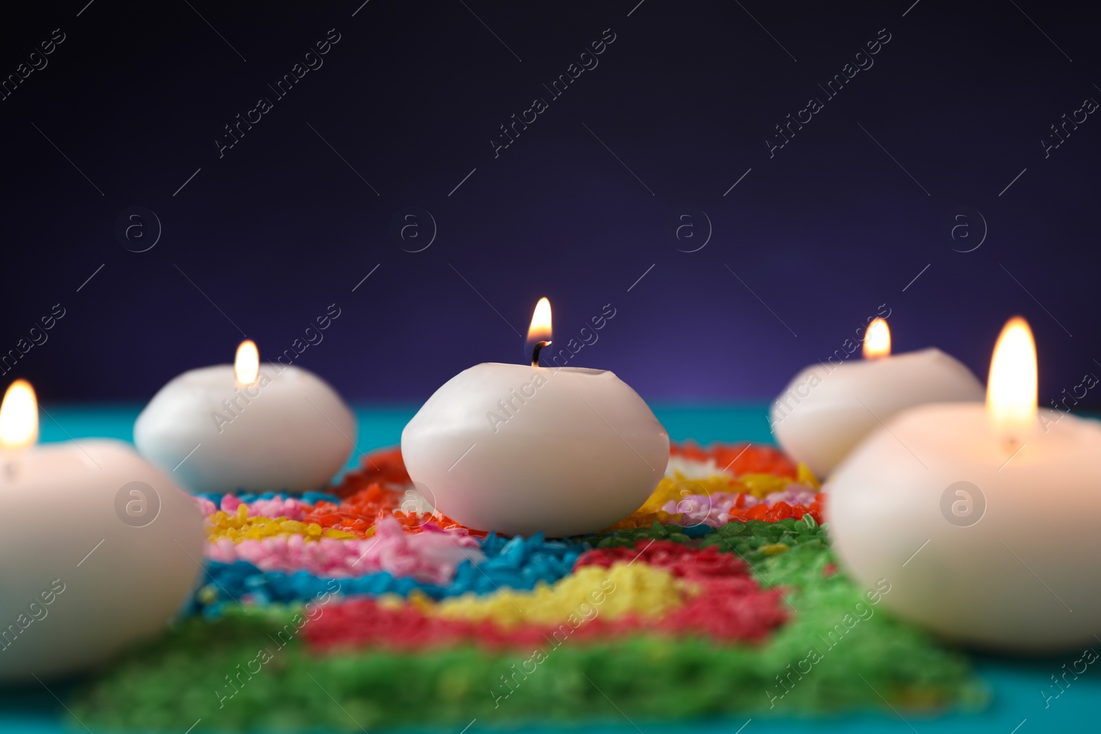 Photo of Diwali celebration. Burning candles and colorful rangoli against purple background, closeup