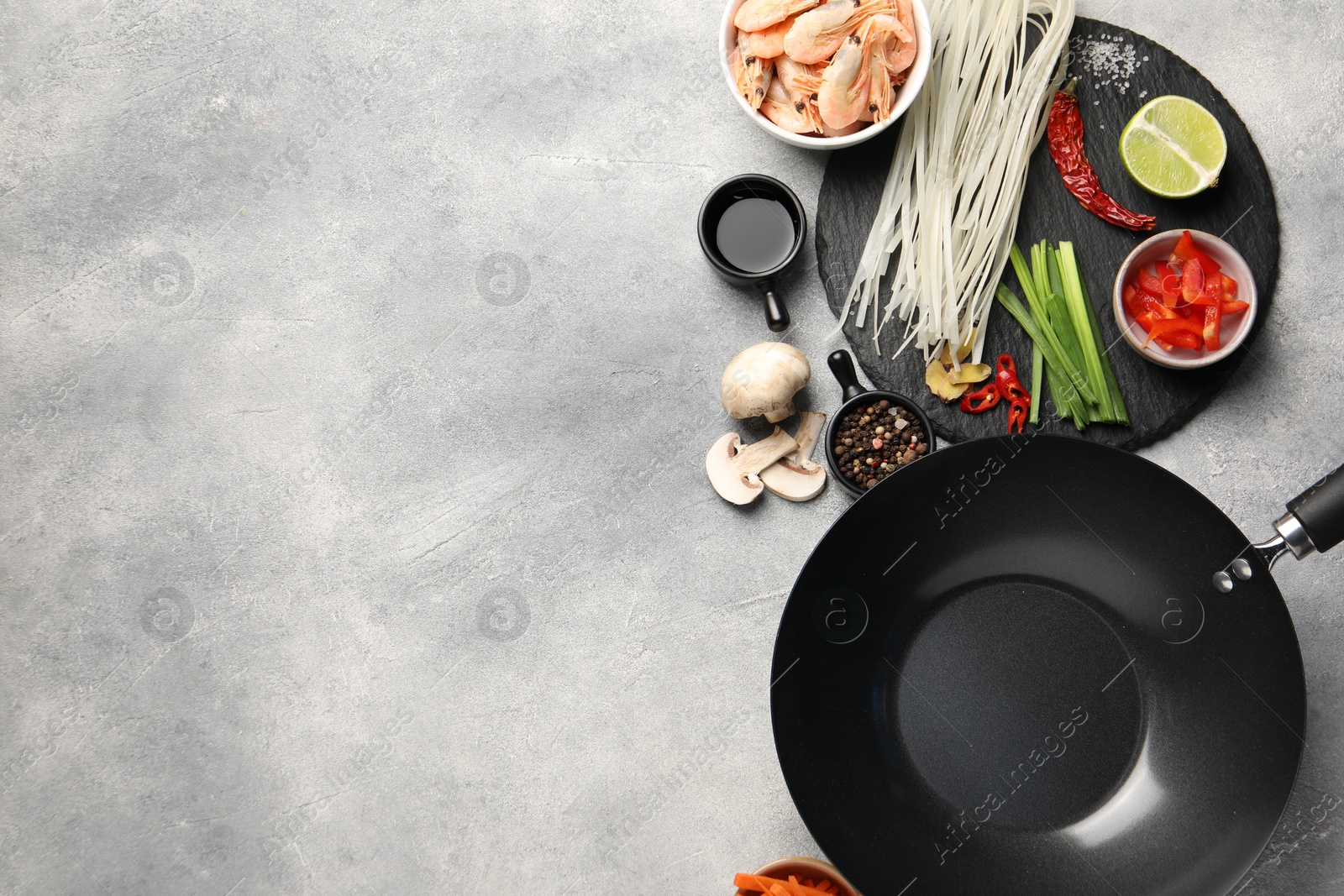 Photo of Flat lay composition with black wok, spices and products on grey textured table. Space for text