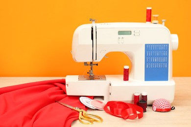 Photo of Modern sewing machine with cloth and craft accessories on wooden table near orange wall