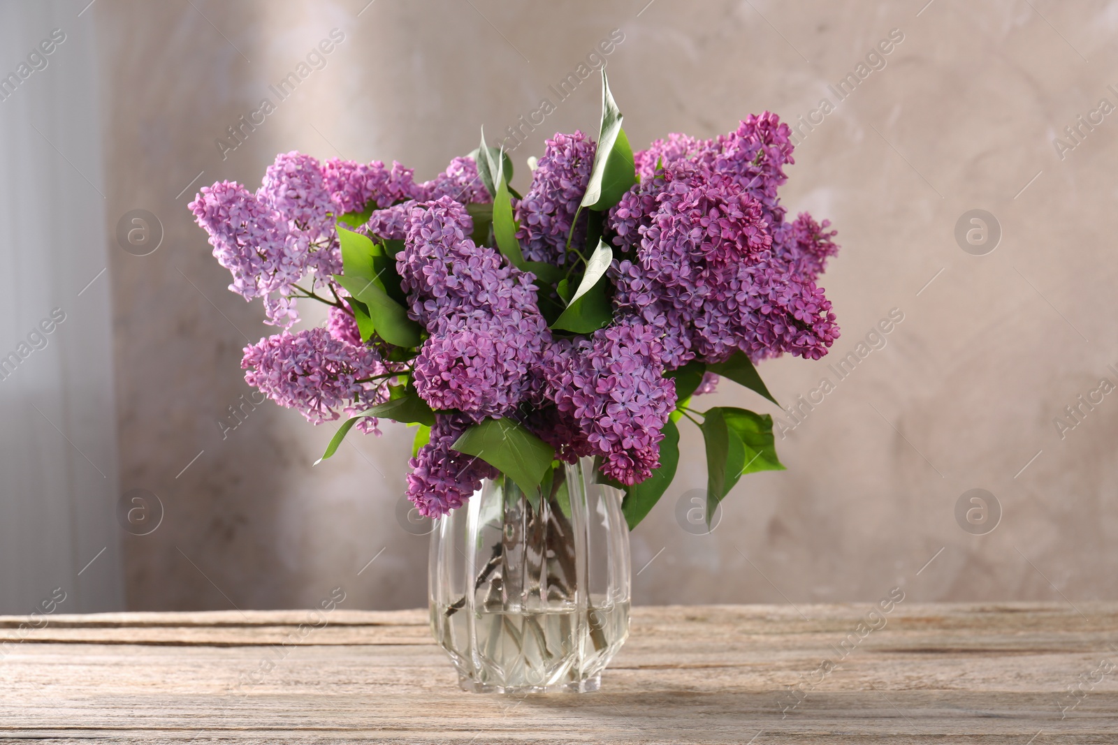 Photo of Beautiful lilac flowers in vase on wooden table