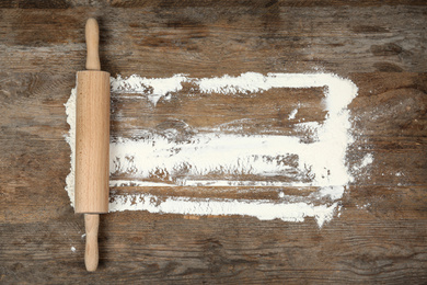 Photo of Flour and rolling pin on wooden table, flat lay