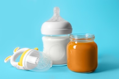 Photo of Jar with healthy baby food, bottle of milk and fruit feeder on light blue background