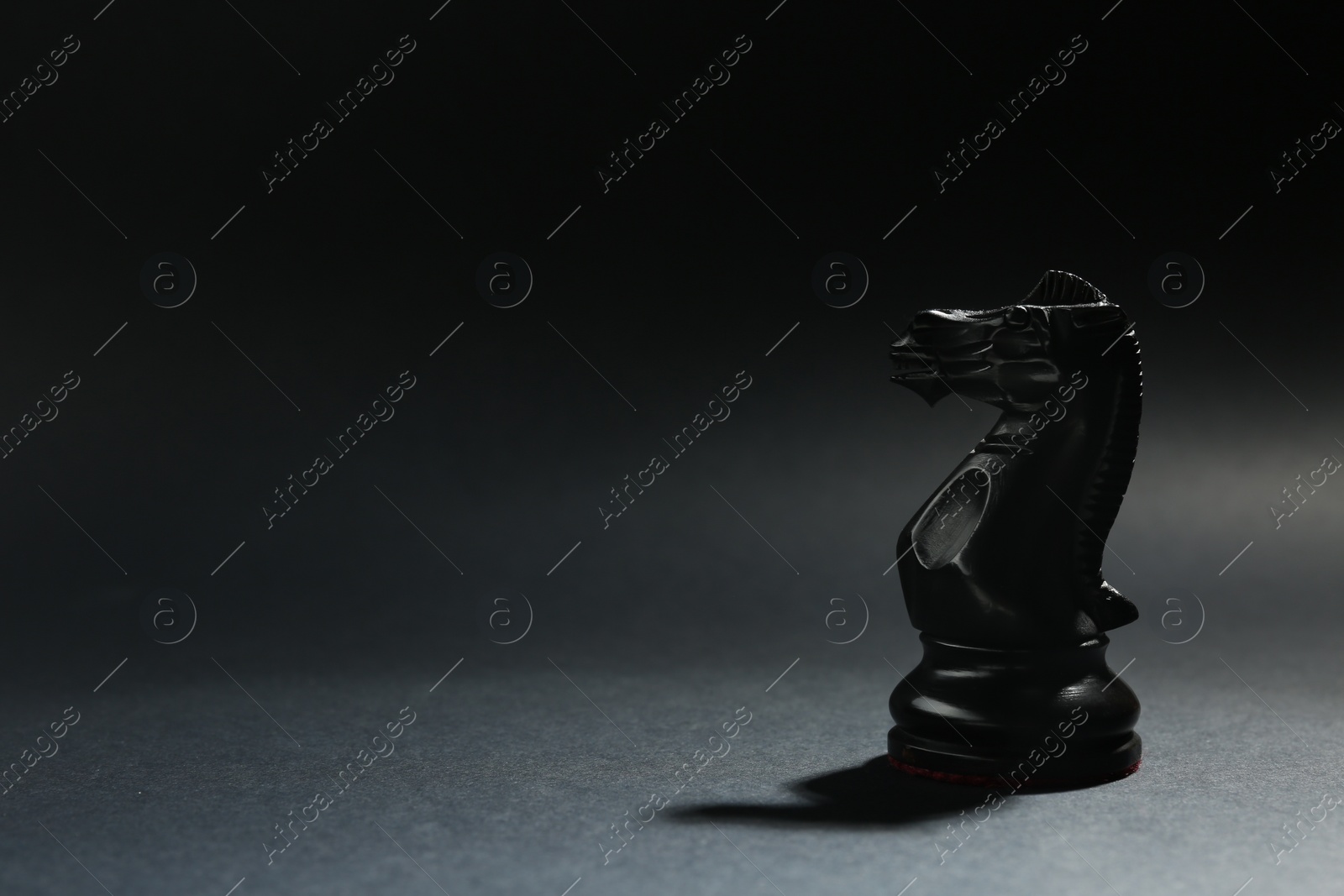 Photo of Black wooden chess knight on dark background. Space for text