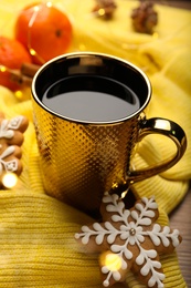 Cup of hot drink with yellow sweater and gingerbread cookie on table, closeup