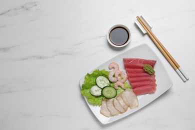 Photo of Sashimi set (raw slices of tuna, oily fish and shrimps) served with cucumber, lettuce, vasabi and soy sauce on white marble table, flat lay. Space for text