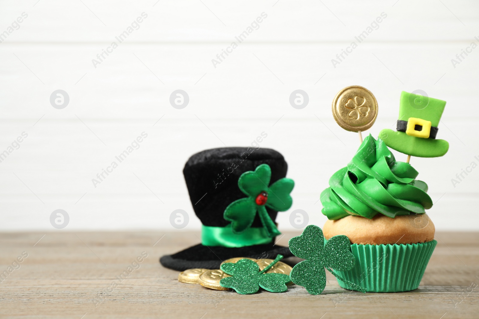 Photo of Decorated cupcake and hat on wooden table, space for text. St. Patrick's Day celebration