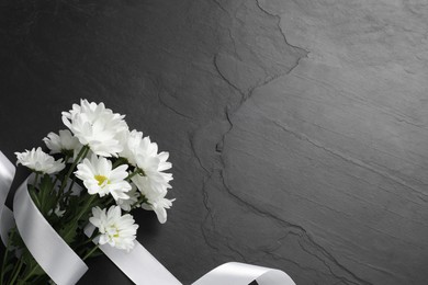 Photo of Beautiful chrysanthemum flowers and white ribbon on black table, top view with space for text. Funeral symbols