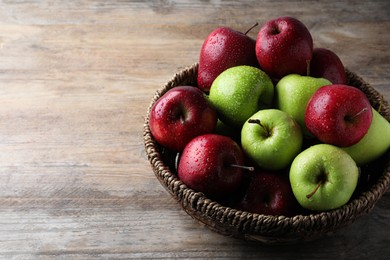 Photo of Fresh ripe green and red apples with water drops in wicker bowl on wooden table, space for text