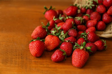 Photo of Basket with scattered ripe strawberries on wooden table, closeup