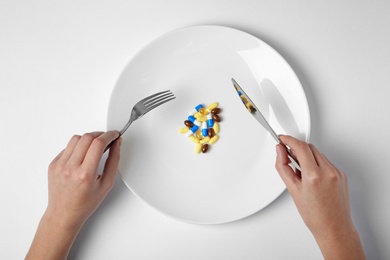 Photo of Woman holding cutlery near plate with weight loss pills on white background, top view