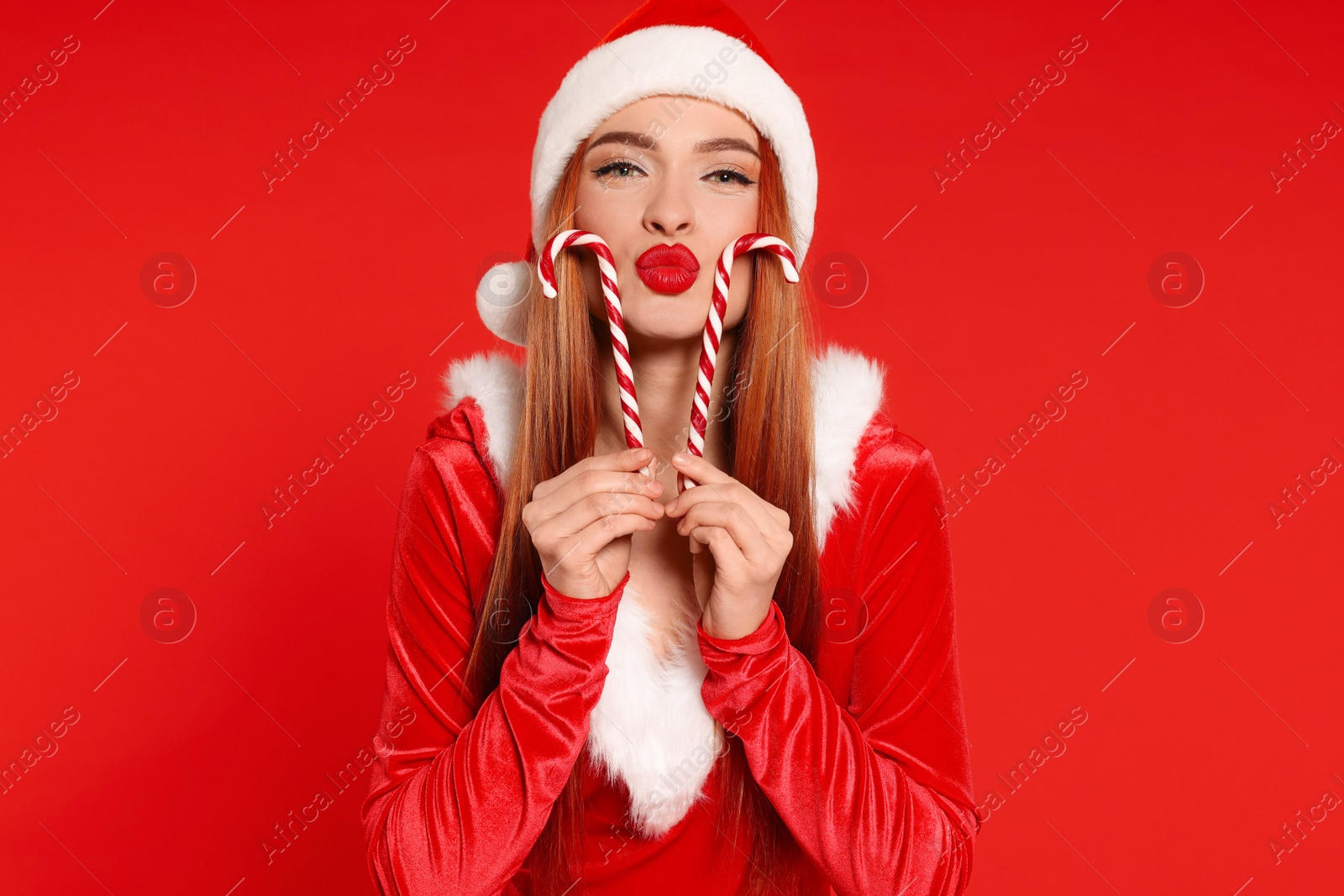 Photo of Young woman in Santa hat with candy canes on red background. Christmas celebration