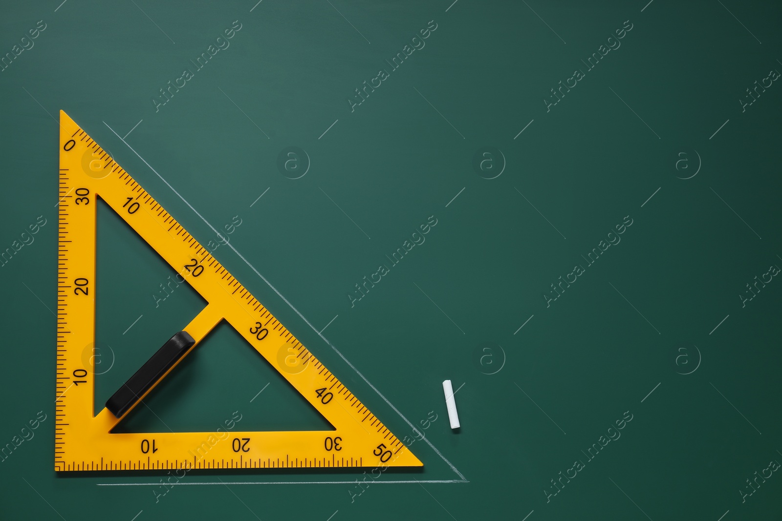 Photo of Yellow triangle and chalk on green chalkboard, flat lay. Space for text