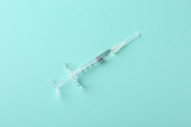 Photo of Injection cosmetology. One medical syringe on turquoise background, top view