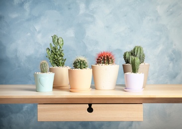 Photo of Beautiful cacti on table against color wall