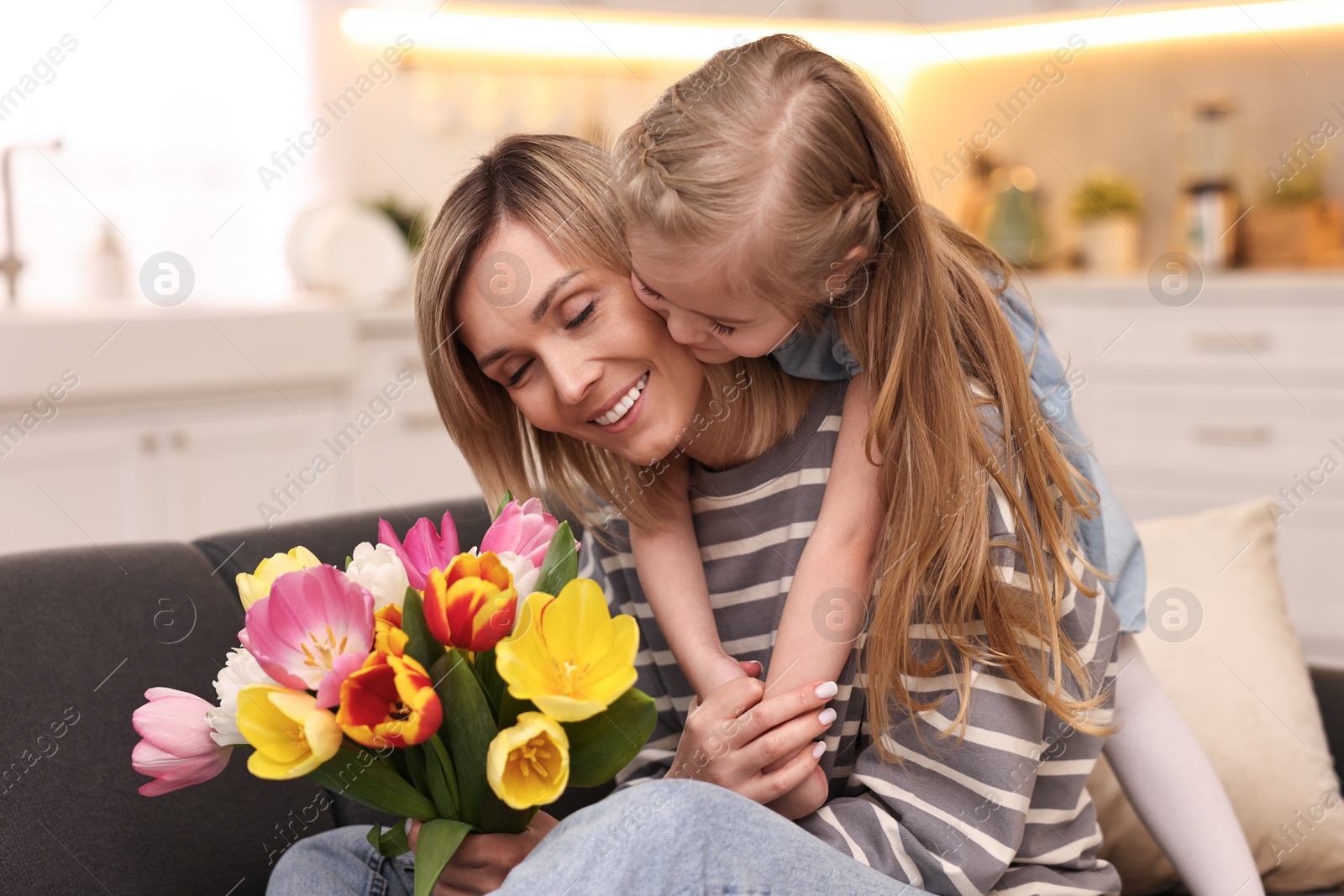 Photo of Little daughter congratulating her mom with Mother`s Day at home. Woman holding bouquet of beautiful tulips