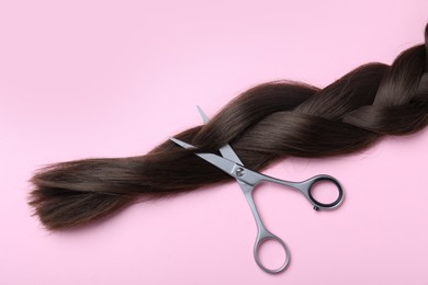 Photo of Professional hairdresser scissors and braid on pink background, flat lay. Haircut tool