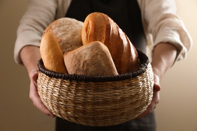 Photo of Man holding wicker basket with different types of bread on beige background, closeup