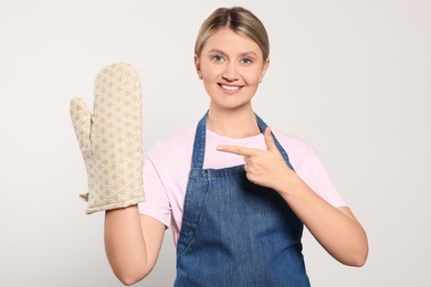 Photo of Beautiful young woman in denim apron and oven glove on light grey background