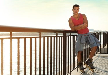 Photo of Handsome young man with roller skates on pier near river, space for text