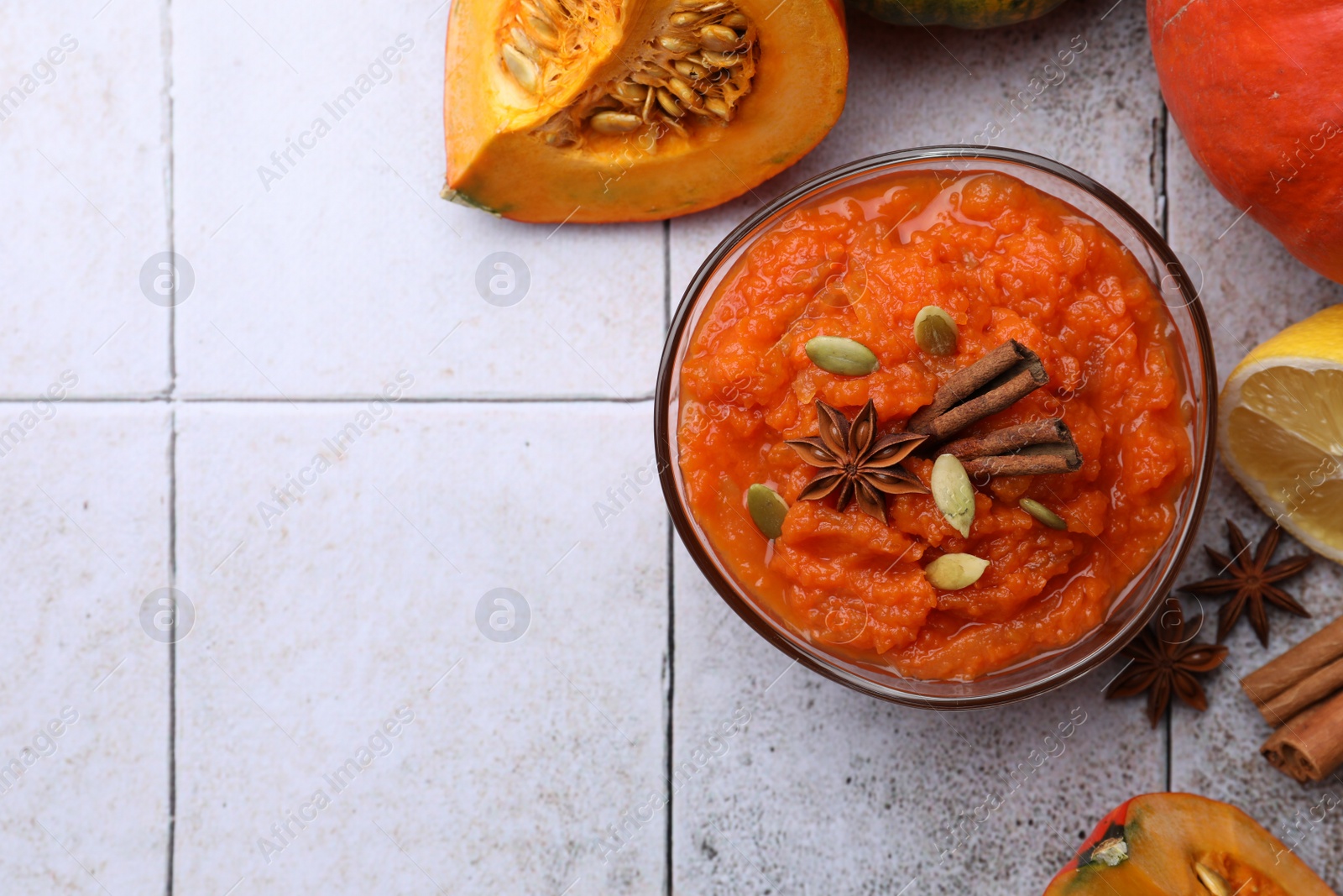 Photo of Bowl of delicious pumpkin jam and ingredients on tiled surface, flat lay. Space for text