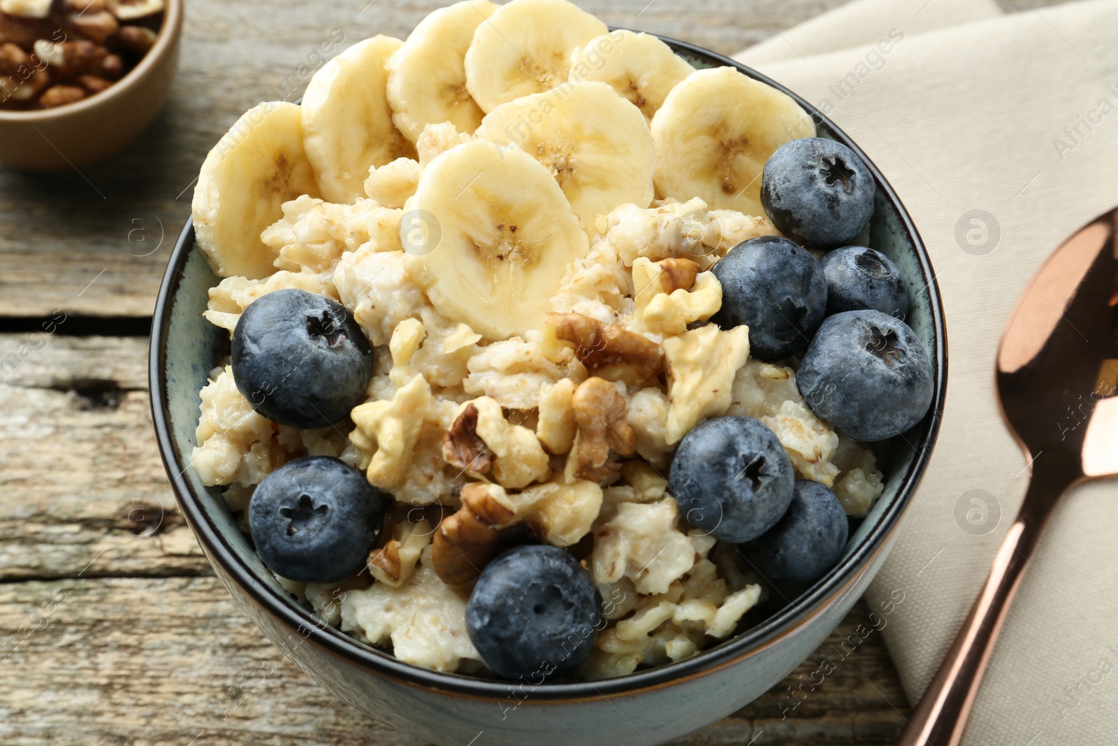 Photo of Tasty oatmeal with banana, blueberries and walnuts served in bowl on wooden table, closeup