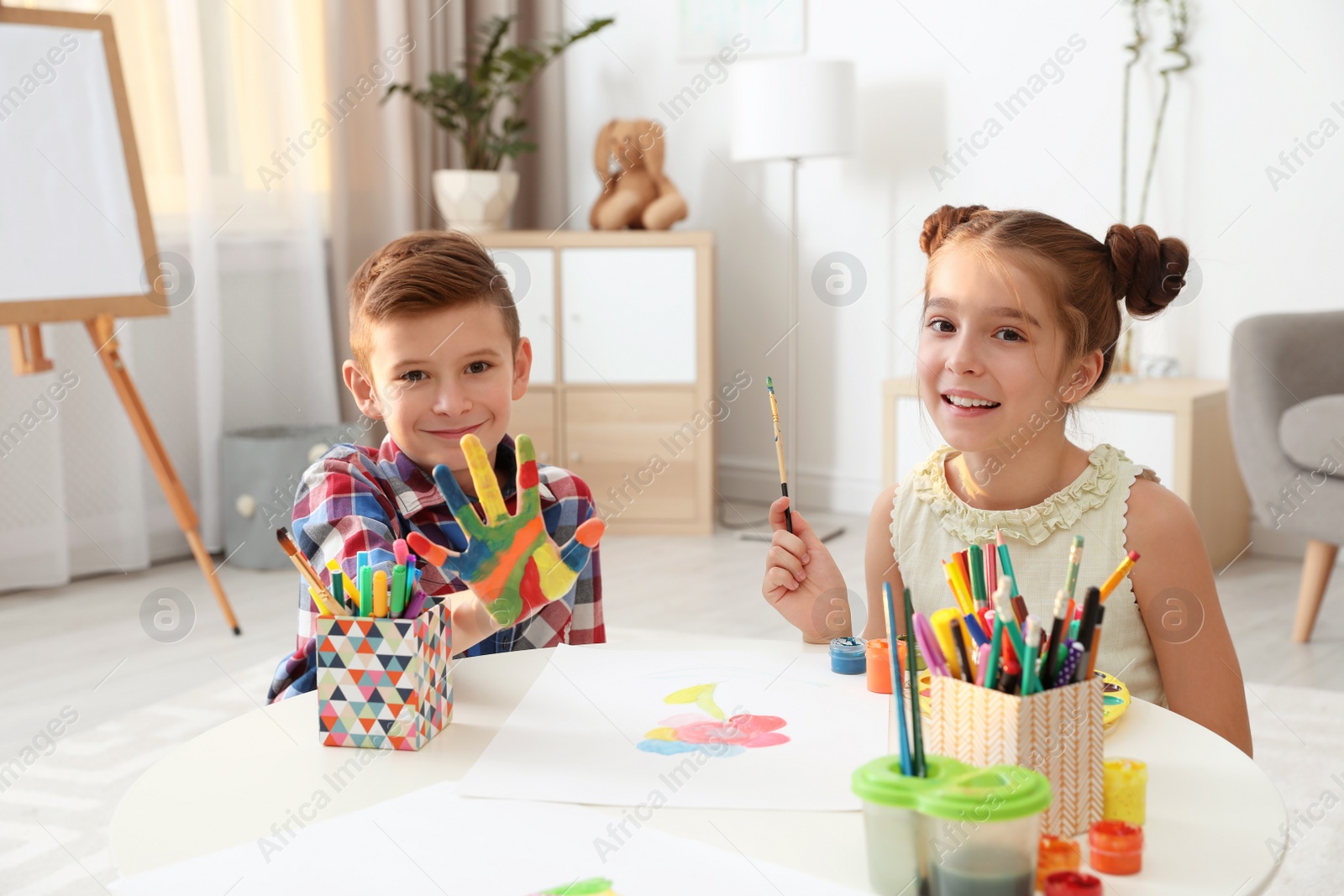 Photo of Little children painting hands at table indoors