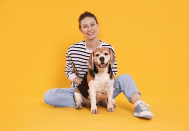 Photo of Happy young woman with cute Beagle dog on orange background. Lovely pet