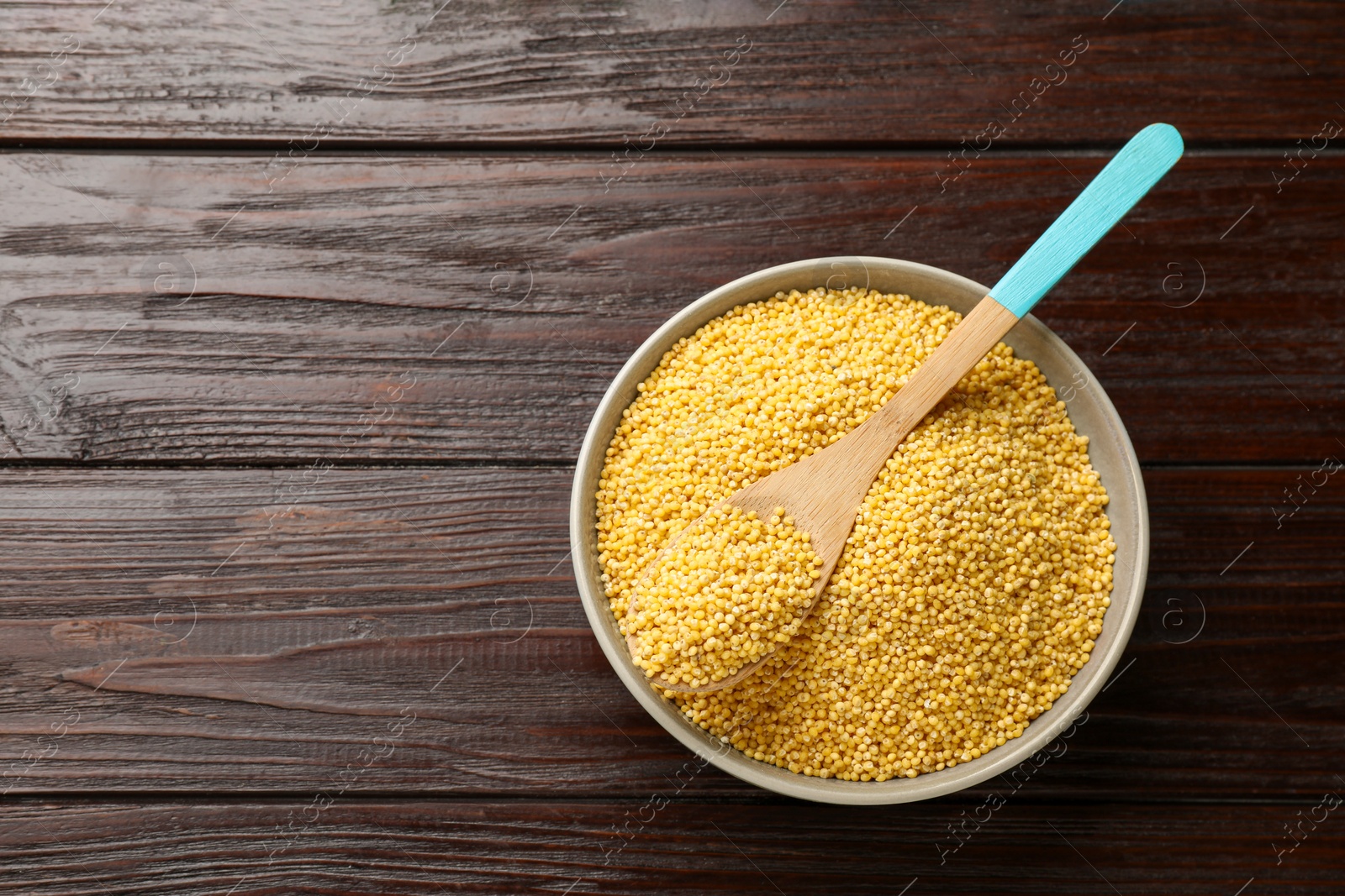 Photo of Millet groats in bowl and spoon on wooden table, top view. Space for text