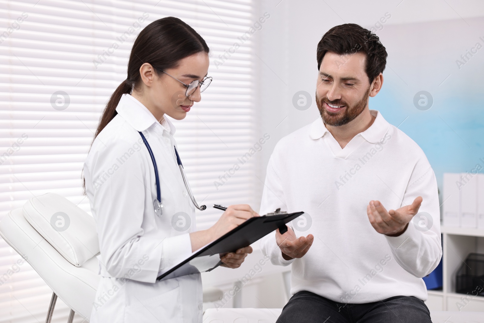 Photo of Doctor with clipboard consulting patient during appointment in clinic