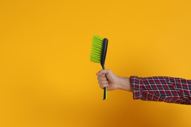 Young man with broom on orange background, closeup. Space for text