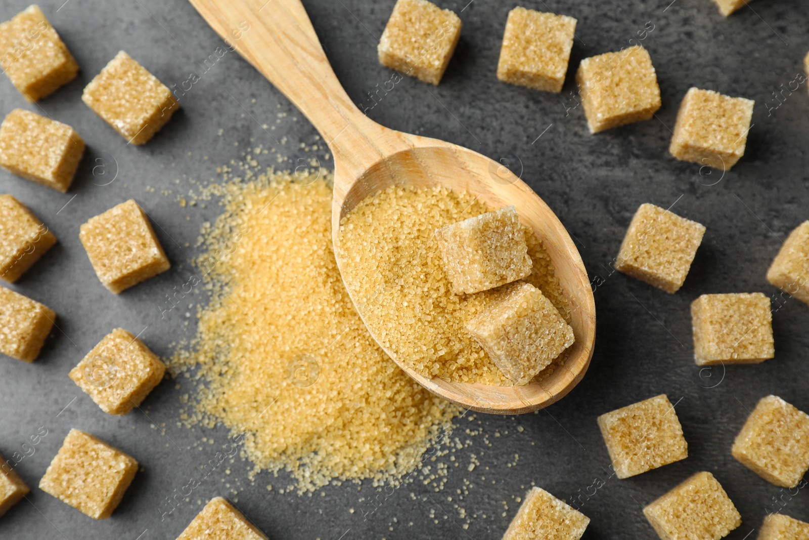 Photo of Spoon with brown sugar cubes on grey table, flat lay