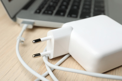 Photo of Charger and laptop on wooden table, closeup. Modern technology