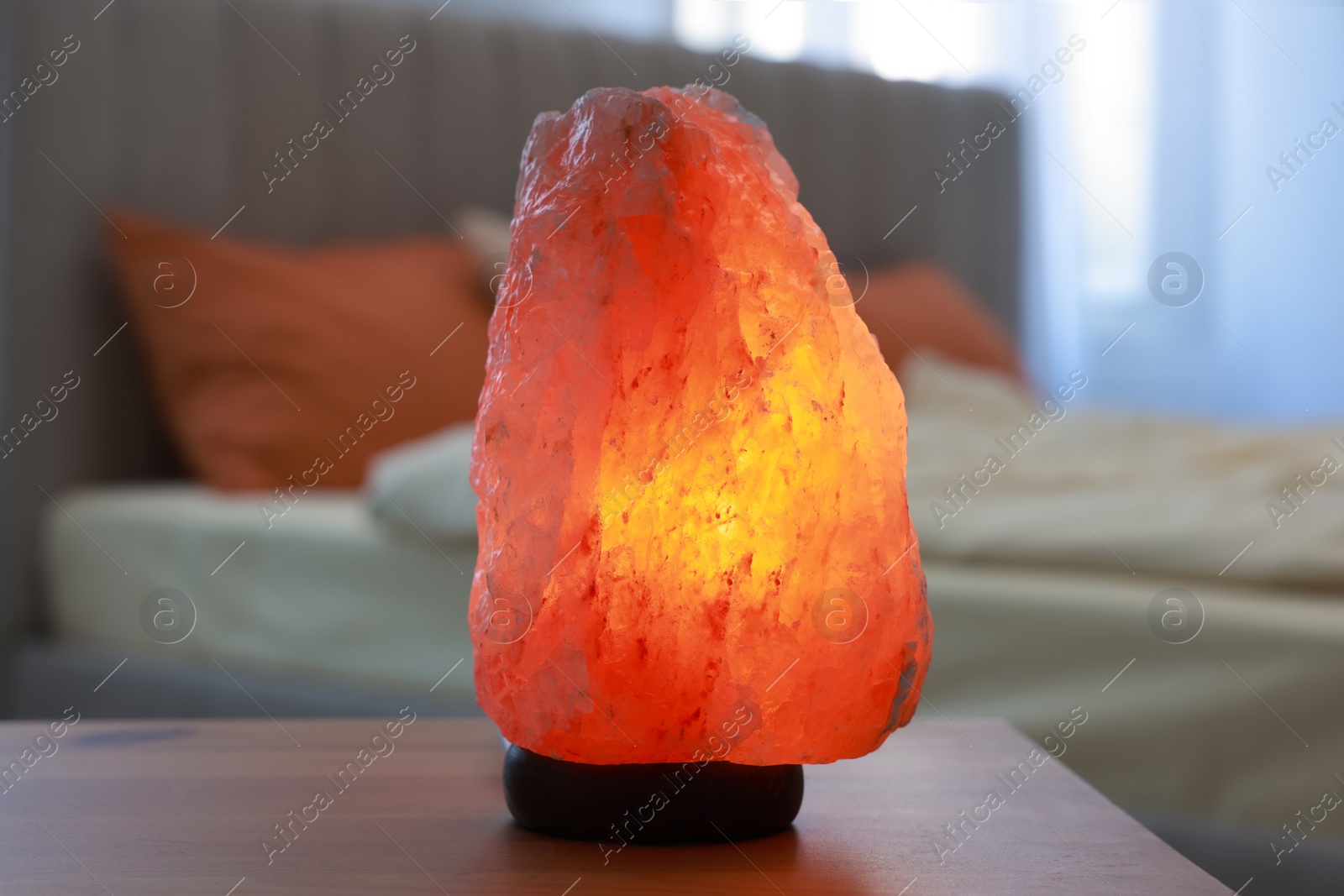 Photo of Himalayan salt lamp on wooden table in bedroom