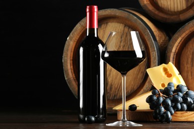 Delicious wine, wooden barrels, cheese and fresh grapes on table, space for text