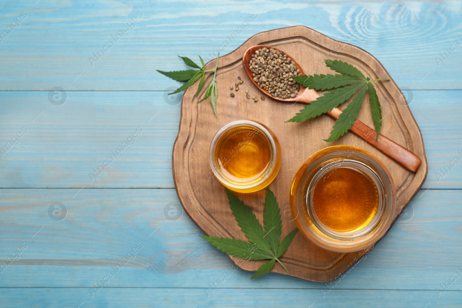 Photo of Hemp oil, seeds and leaves on light blue wooden table, flat lay. Space for text