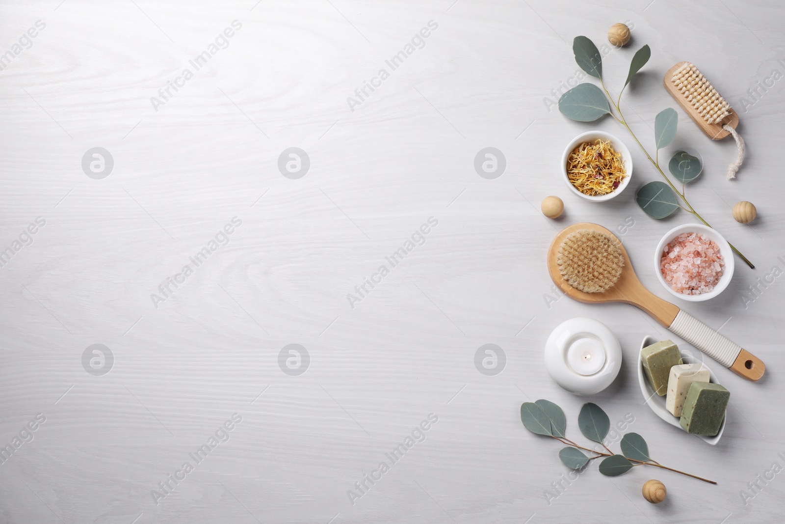 Photo of Flat lay composition with different spa products, burning candle and eucalyptus branches on light wooden table. Space for text