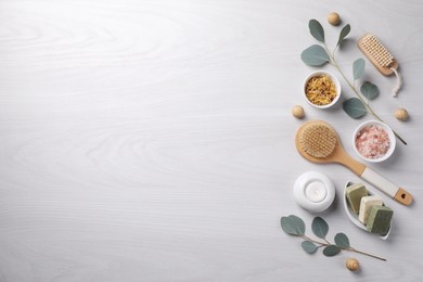 Flat lay composition with different spa products, burning candle and eucalyptus branches on light wooden table. Space for text