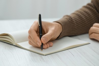 Man writing in notebook at white wooden table, closeup