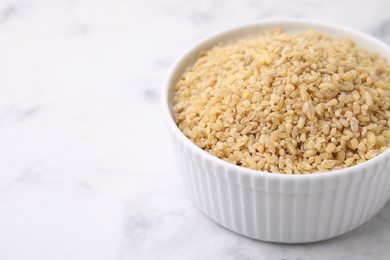 Photo of Raw bulgur in bowl on light table, closeup. Space for text