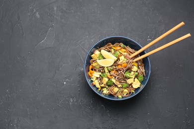 Photo of Stir-fry. Delicious cooked noodles with chicken and vegetables in bowl served on gray textured table, top view. Space for text