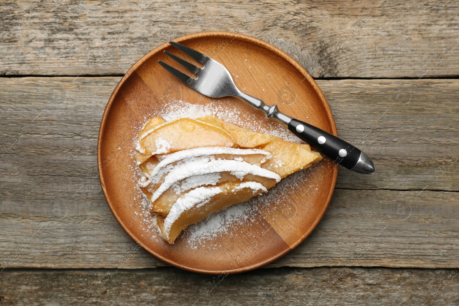 Photo of Piece of tasty homemade quince pie with powdered sugar and fork on wooden table, top view