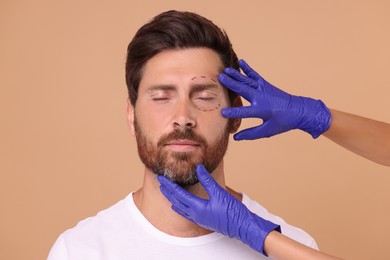 Doctor checking marks man's on face for cosmetic surgery operation against beige background