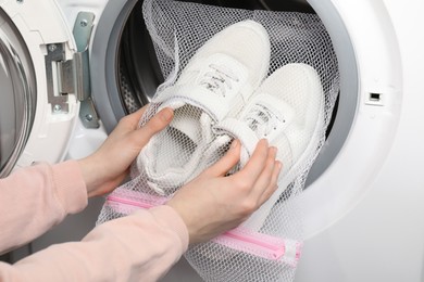 Photo of Woman putting stylish sneakers into washing machine, closeup